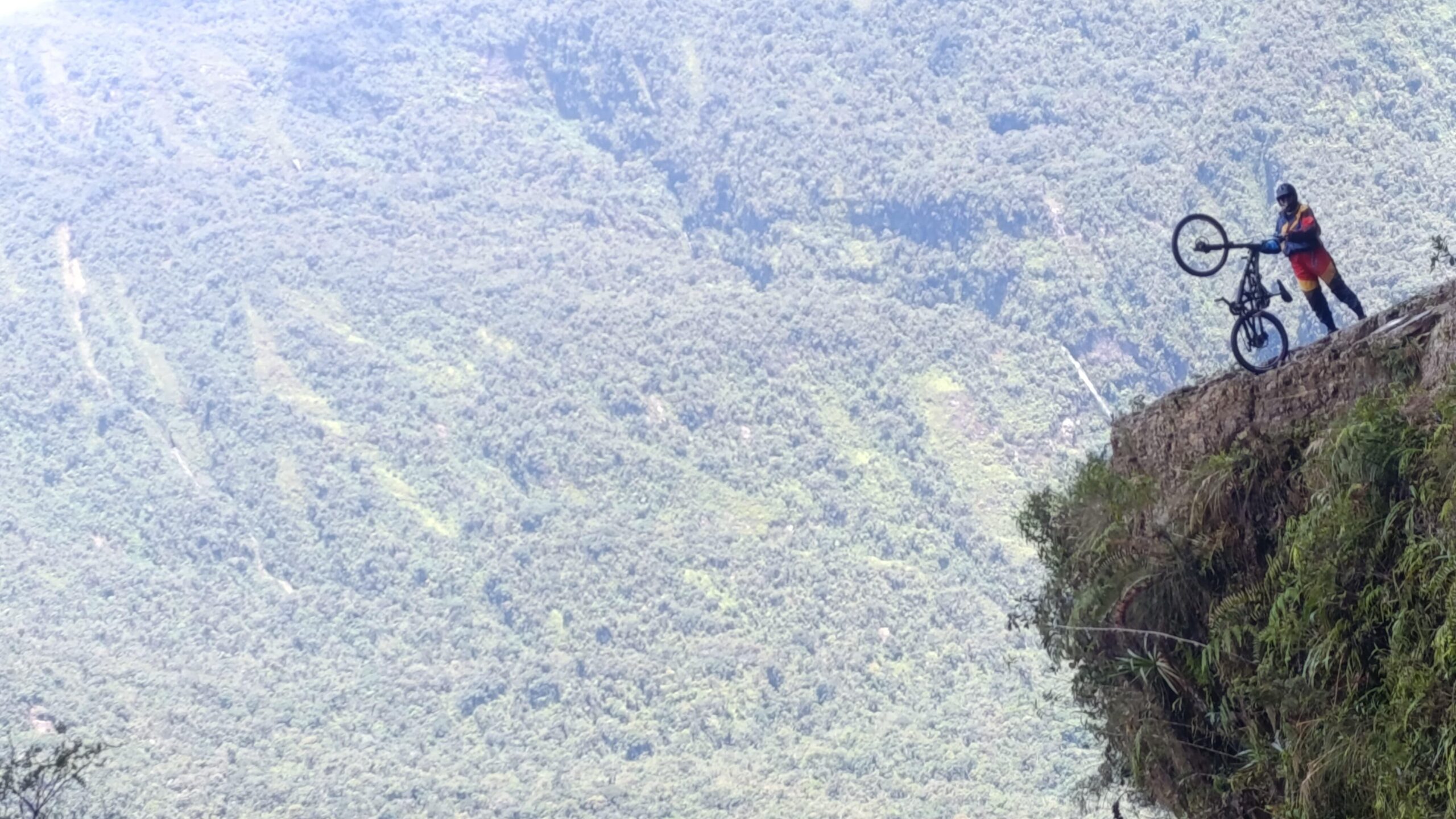 Woman wearing a cycling helmet holding a bike over the edge of a cliff on Bolivia's Death Road.